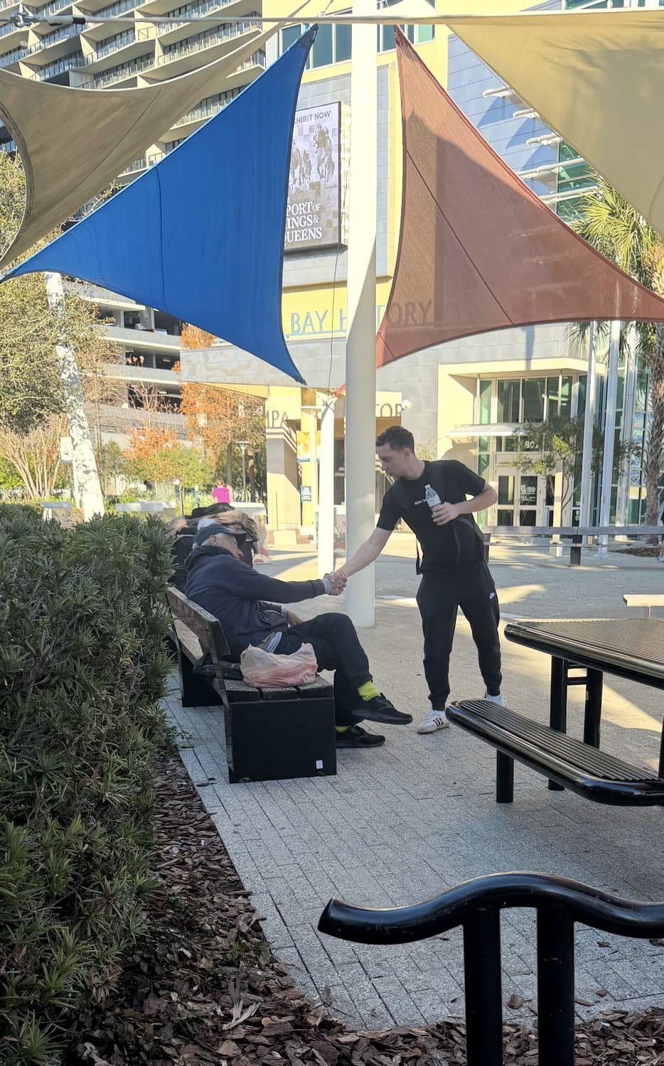 A volunteer shaking hands with a man on a bench while handing him water